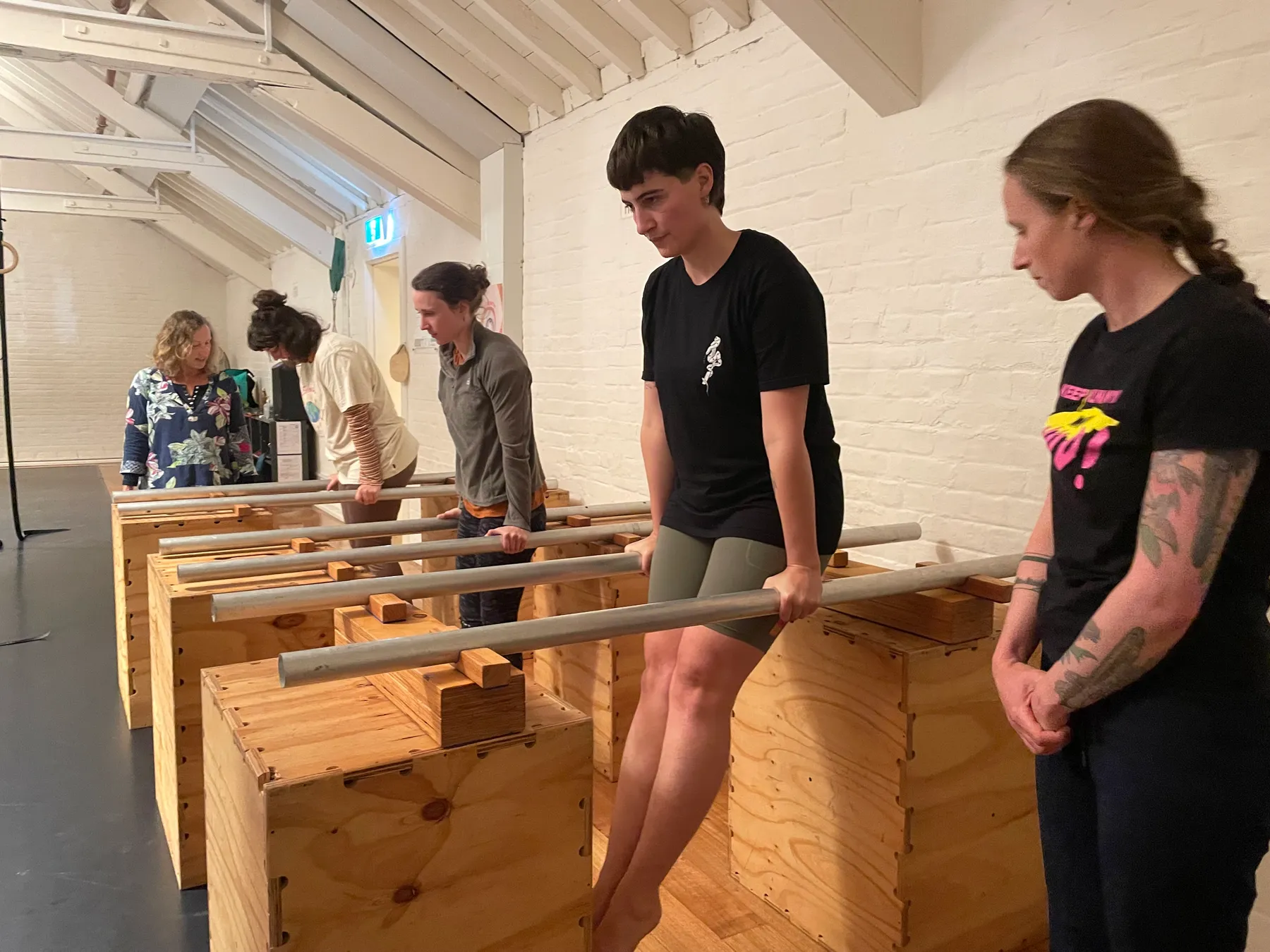 Two students holding themselves up on parallel bars set over plywood boxes, a coach watching alongside