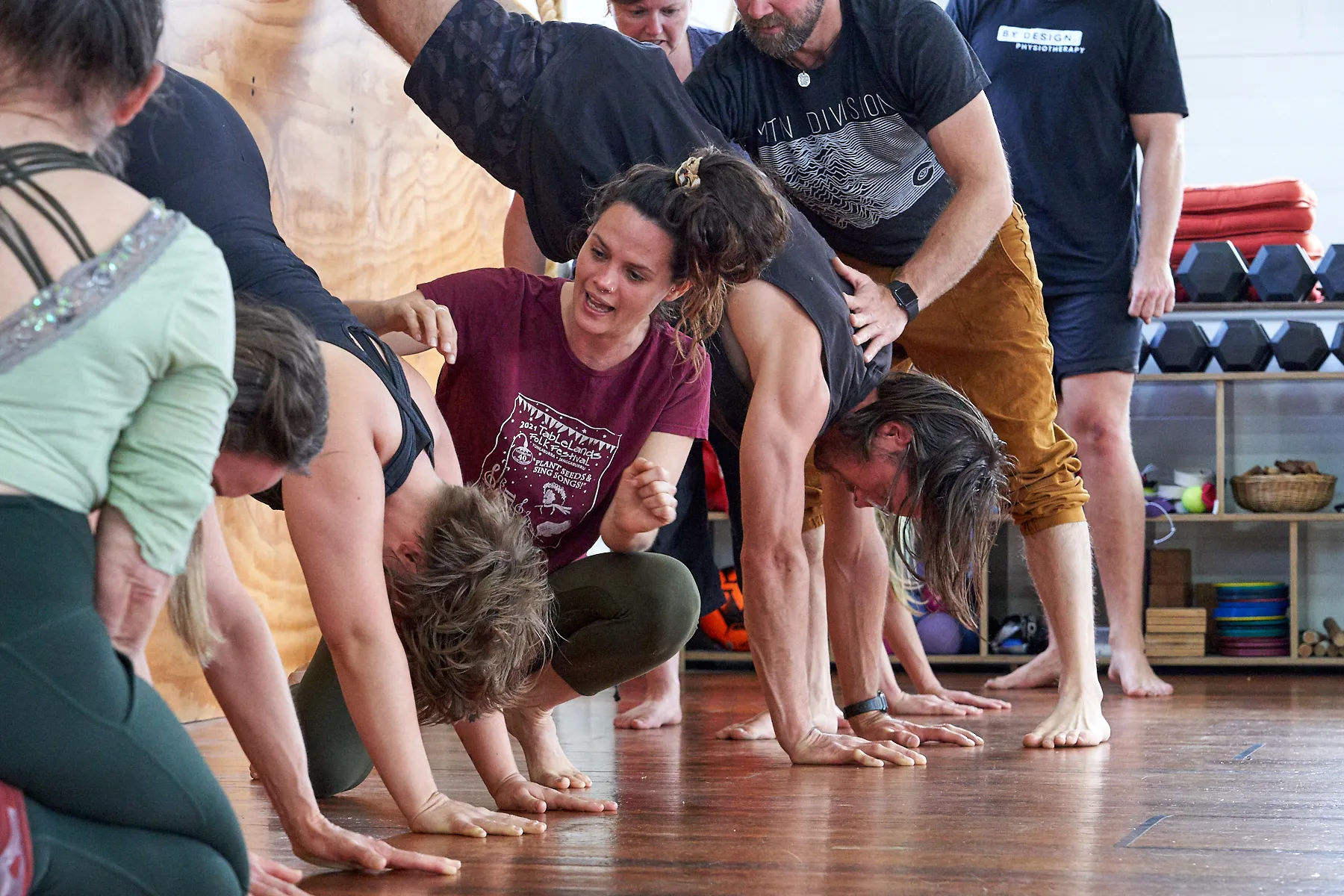 A coach crouched mid-cue beside a row of students folded forward with their hands on the studio floor