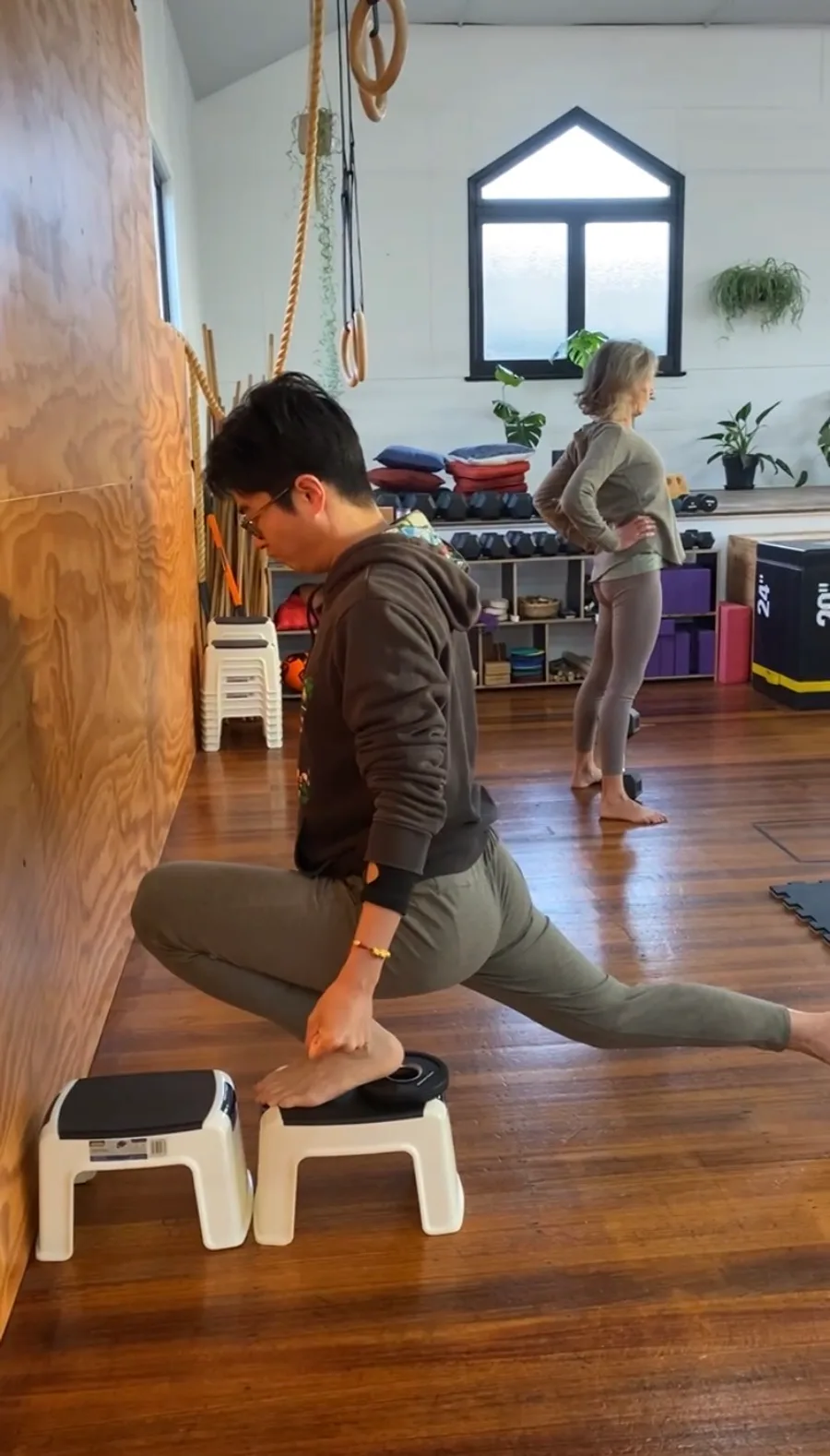 A student in a deep low lunge with both hands pressing into low steps, another mover working behind them