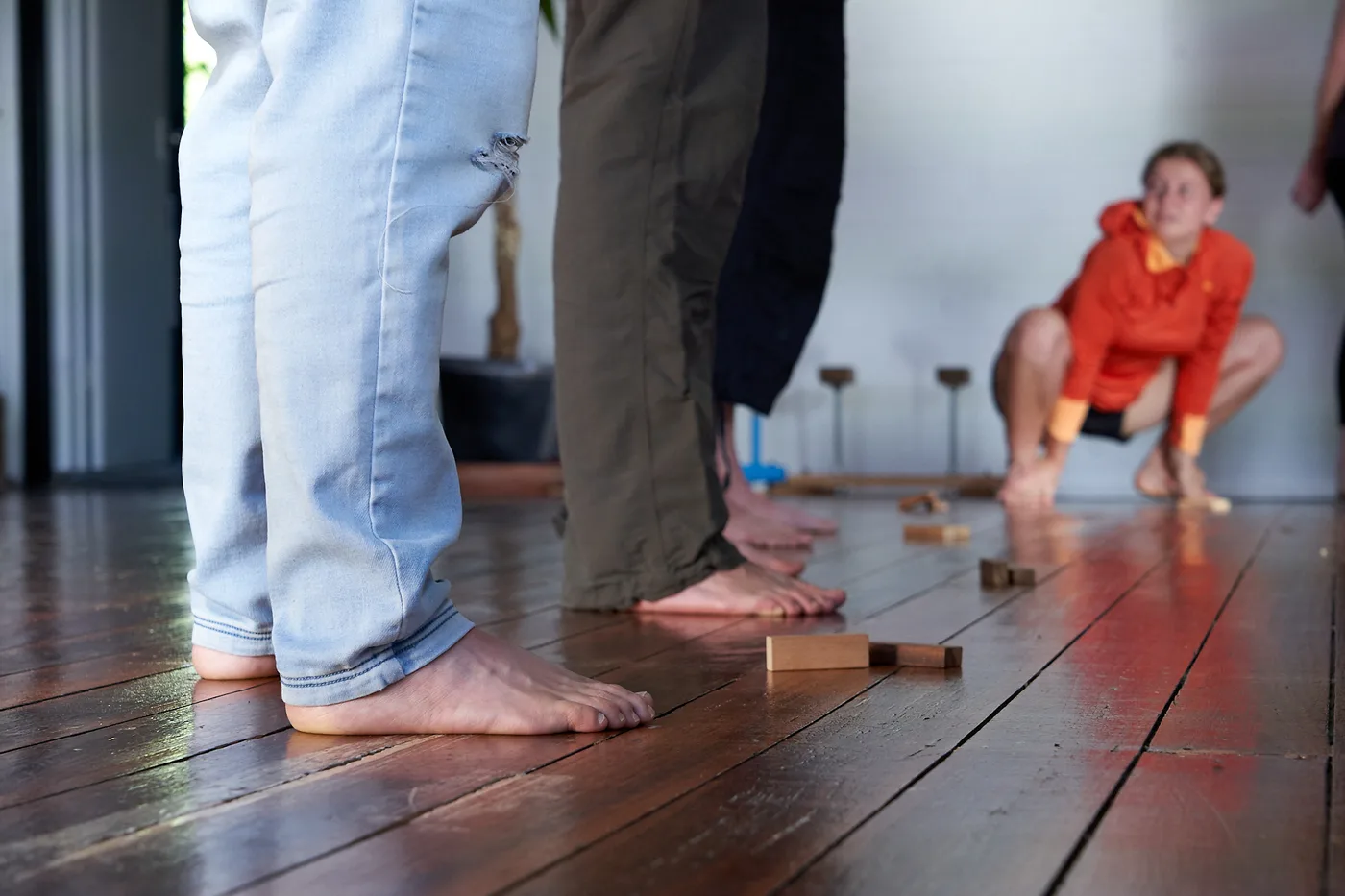 Bare feet on the wooden studio floor, a student holding a deep resting squat in the background