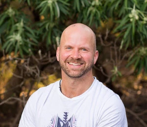 Scott, founder of Totum Movement, smiling in front of native garden greenery